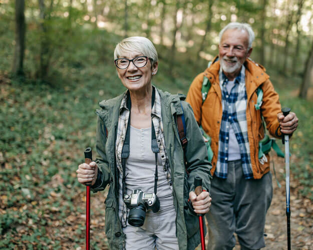 Älteres Paar wandert mit Nordic Walking Stöcken durch den Wald